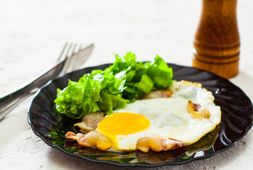 fried eggs with bacon and salad in black plate on white table