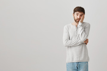 Hold long do I need to listen to this stupid guy. Portrait of bored and amazed male student leaning head on palm while standing over gray background, being fed up of politician speech