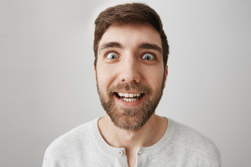 Close-up portrait of funny bearded guy making faces at camera, smiling and acting like crazy,...