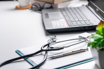 Laptop / stethoscope and clipboard on white table soft focus