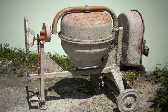 Rarely used Cement mixer standing near a wall. Cement mixers, or concrete mixers, allow users to mix large amount of cement, sand, or gravel with water.