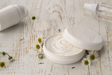 Obraz na płótnie Canvas Natural cosmetics for face and body skin care. A round jar with cream and fresh chamomile flowers on a light wooden background. 