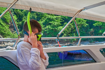 Boy dresses a mask for scuba diving. Side view,  in ocean yacht against a background of green dense...