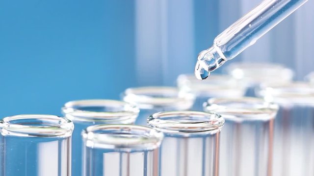 The liquid in a pipette drips into test tubes. Close up.