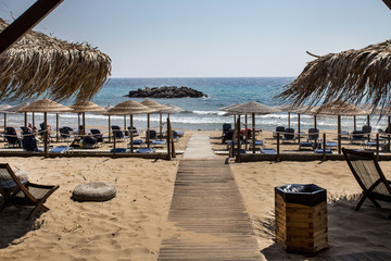 A resort with plenty of place to relax under shady umbrellas, made of palm leaves. There is a wooden pathway leading from the entrance to the shady relaxing area.
