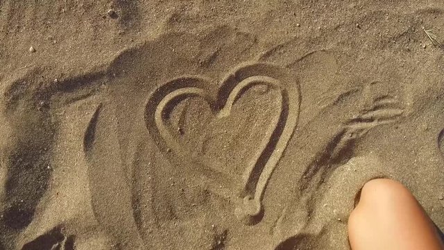 Woman Hand Draws a Heart on the Sandy Shore