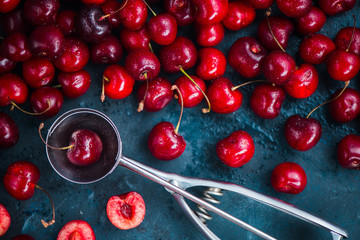 Cherries and ice cream spoon on a grey concrete background, summer berries concept with copy space. Making dessert flat lay in neutral color tones