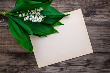 Lily of the valley bouquet and a sheet of paper on a wooden surface