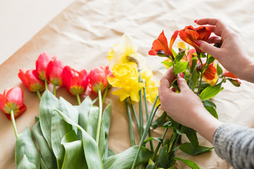Fototapeta na wymiar florist at work. woman hands arranging a spring flower bouquet from assortment of alstroemeria red tulips and narcissus