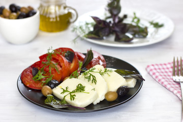 White cheese with tomatoes, green and black olives, basil, coriander and olive oil on a black plate