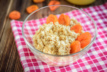Oatmeal porridge with dried apricot, raisins and honey in bowl on dark wooden background. Healthy food for breakfast.