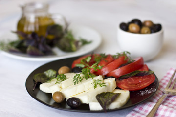 White cheese with tomatoes, green and black olives, basil, coriander and olive oil on a black plate