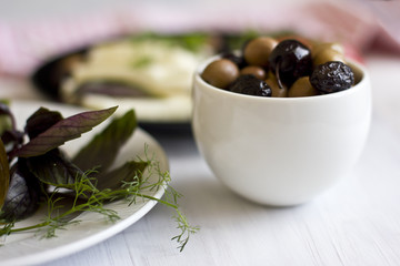 White cheese, green and black olives, basil, coriander and olive oil on a black plate