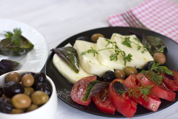 White cheese with tomatoes, green and black olives, basil, coriander and olive oil on a black plate