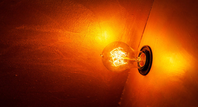 Glowing orange light bulb in the dark with copy space