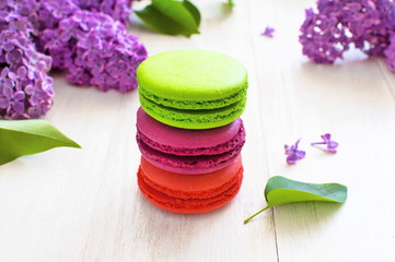 Sweet colorful french macaroons and spring lilac flowers on white wooden background. Beautiful dessert Colorful almond cookies Pastel colors Bouquet of lilacs