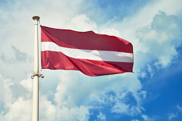 Fototapeta na wymiar National flag of Latvia on flagpole against cloudy sky