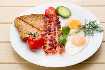 Fried eggs with bacon on the wooden table.