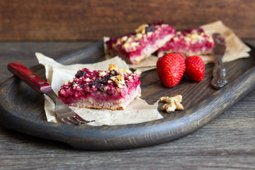 Stack of cake or cookies with strawberry, chocolate and walnuts with sweet crumbs (streusel) on a parchment paper, selective focus. Strawberry bars. Square shape. Traditional mix of flavors