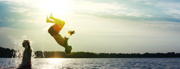 Glückliche junge Menschen laufen und springen am See beim Sonnenuntergang