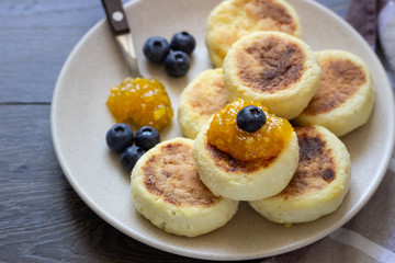 Cottage cheese pancakes (syrniki) with sour cream, orange jam and fresh blueberries on a plate. Breakfast or lunch concept. 