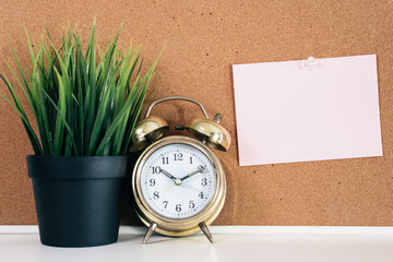 Blank paper note on cork board with golden alarm clock and green plant in pot. memo and time management concept. blank note for copy space or typography