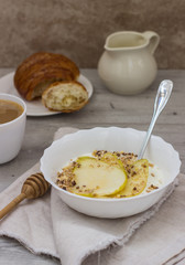 Healthy breakfast bowl: yogurt with pears, honey and granola on wooden background