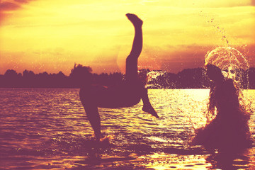 Glückliche junge Menschen laufen und springen am See beim Sonnenuntergang