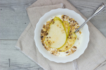 Healthy breakfast bowl: yogurt with pears, honey and granola on wooden background