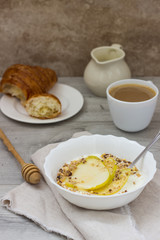 Healthy breakfast bowl: yogurt with pears, honey and granola on wooden background