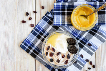 Chocolate layered whipped cottage cheese with honey, raisins and prune on white wooden background. Healthy food for breakfast.