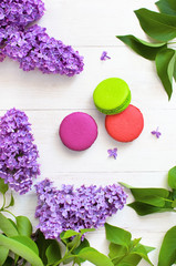Sweet colorful french macaroons and spring lilac flowers on white wooden background. Beautiful dessert Colorful almond cookies Pastel colors Bouquet of lilacs