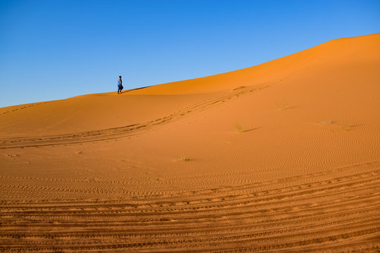 Lonely walker through the desert leaving a trail of footprints. Photograph taken somewhere in the Sahara desert in Merzouga (Morocco)