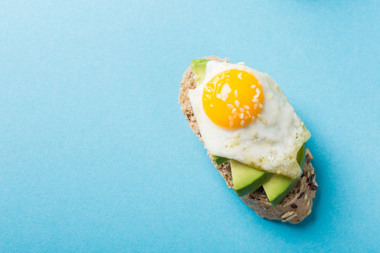 Flat Lay With Healthy Sandwich With Fresh Avocado And Fried Quail Egg On Blue Background. Breakfast Or Lunch Food Concept With Copy Space. Top View.