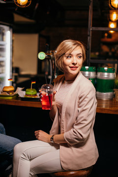 fashion interior photo of beautiful caucasian woman with blond hair drinking delicious beverage in a cosy night club
