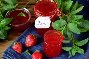 Strawberry jam in glass jars surrounded by the berries and mint