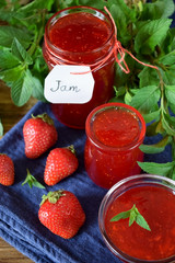 Strawberry jam in glass jars surrounded by the berries and mint
