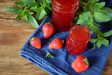 Strawberry jam in glass jars surrounded by the berries and mint