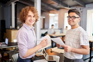 Young men with papers and notepad planning work and discussing organization moments in office