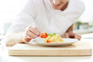 Young chef decorating pasta with fresh tomato pieces before serving