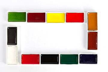 Fototapeta premium Colorful solid watercolor pans set making a frame with copy space on white background