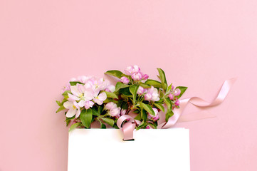 Flat lay top view White gift bag and spring flowers on a pink background. Greeting card with delicate flowers Pink floral background