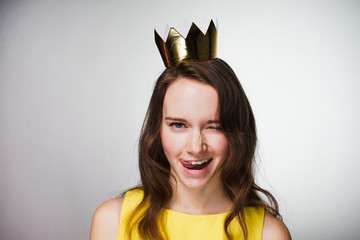 funny young girl in a yellow dress smiles and flirts, on her head a golden crown