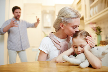 Young woman comforting little daughter while her husband shouting near by