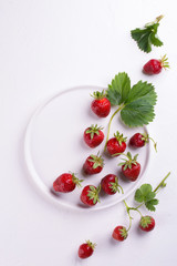 Fresh red strawberry in a bowl with green leaf on white background. Top view