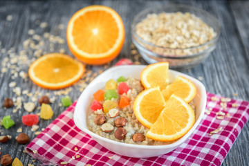 Homemade oatmeal porridge with orange, candied fruit and hazelnut on grey wooden background. Healthy breakfast.