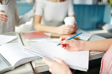 Female hand with pencil over blank page of copybook before sketching or making notes