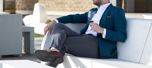 Man millionaire in expensive custom tailored suit, sitting outdoors with glasses and holding a...