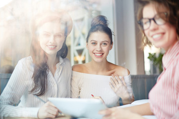 Group of happy girls looking at camera while preparing for project or just searching through internet