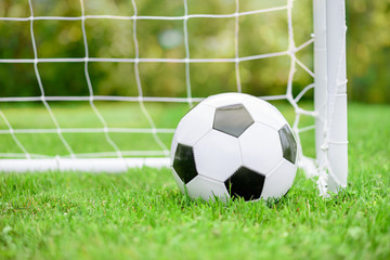Fototapeta na wymiar Classic football (soccer) ball on green grass ground in front of white goal with net